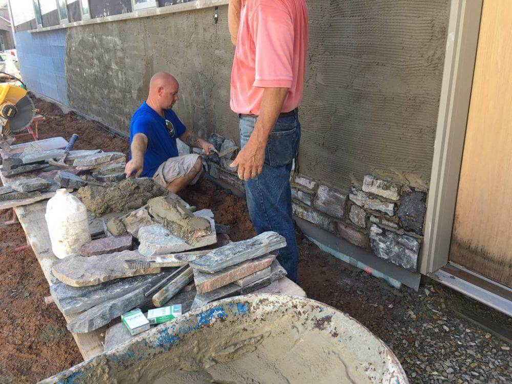 An installation crew installs stone veneer onto a wall.