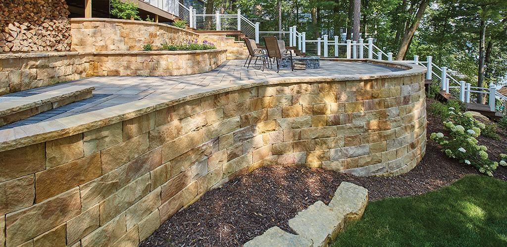 A curved natural stone retaining wall separates an elevated bonfire area from the sloping yard below.