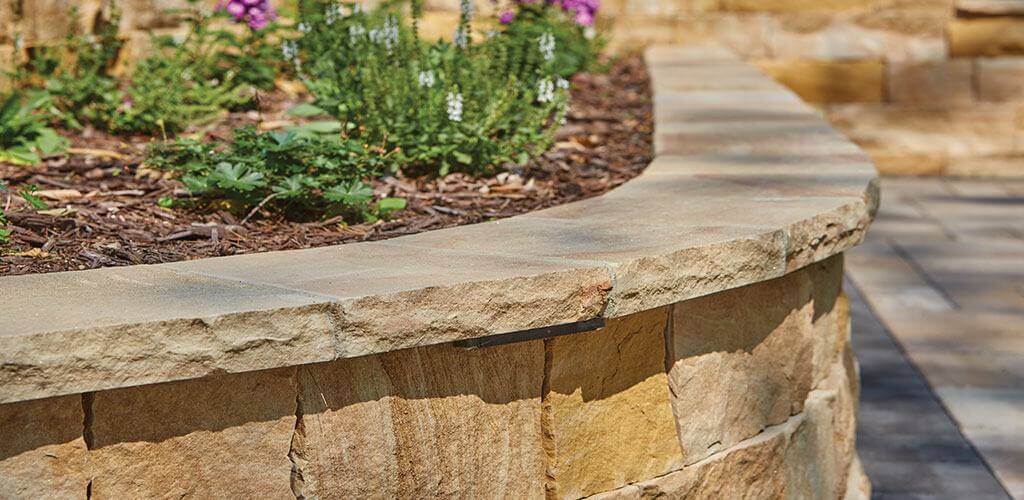 A stone retaining wall curves around some elevated landscaping.