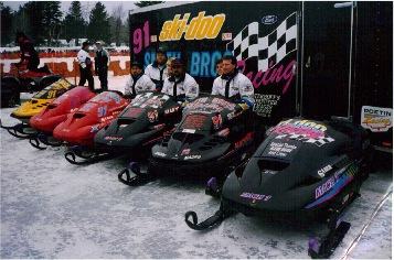 A series of black, red and yellow racing snowmobiles are lined up.