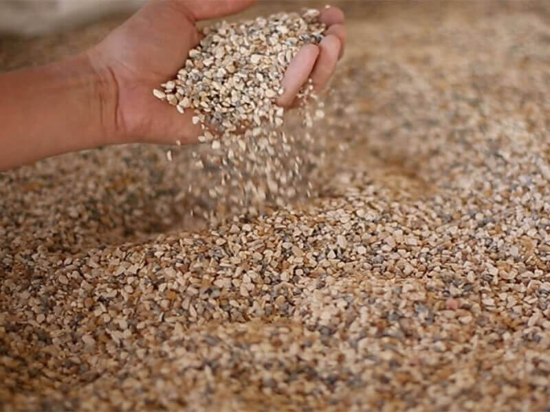A hand sifts through a large container of crushed stone pebbles.