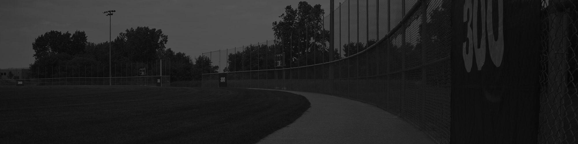 A darkened landscape photo of a baseball field is shown, focused on the warning track.