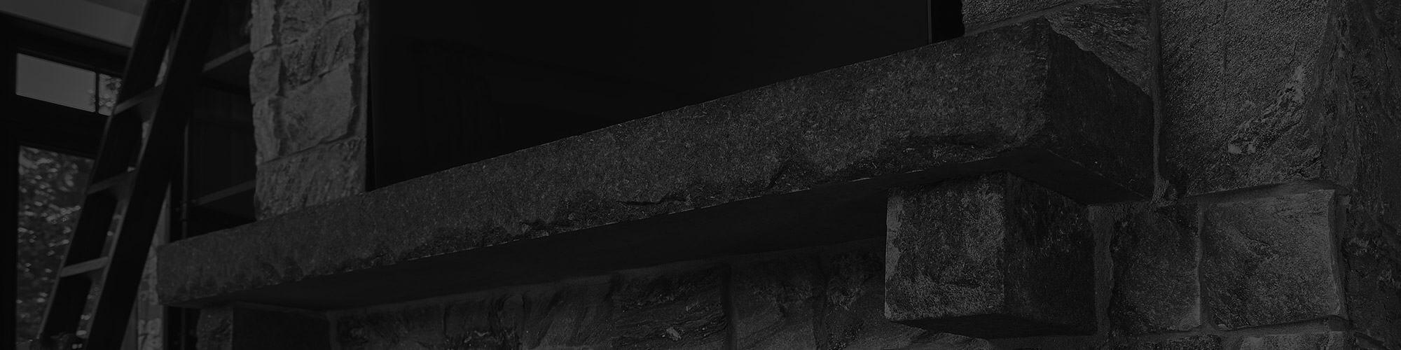 A dark black and white picture of a natural stone fireplace mantel.