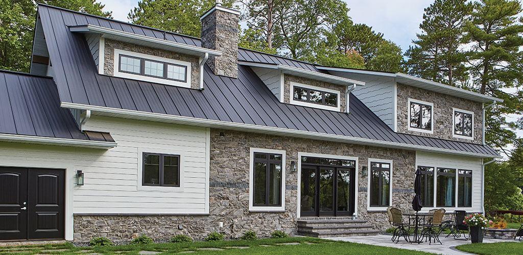 The exterior of a modern farmhouse is shown, using extensive Galaxy Glitter Thin Stone Veneer in a castle cut.